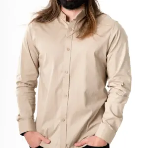 Camisa de popelina beige manga larga con cuello neru y ajuste slim fit, mostrada en modelo masculino de frente con las manos en los bolsillos.