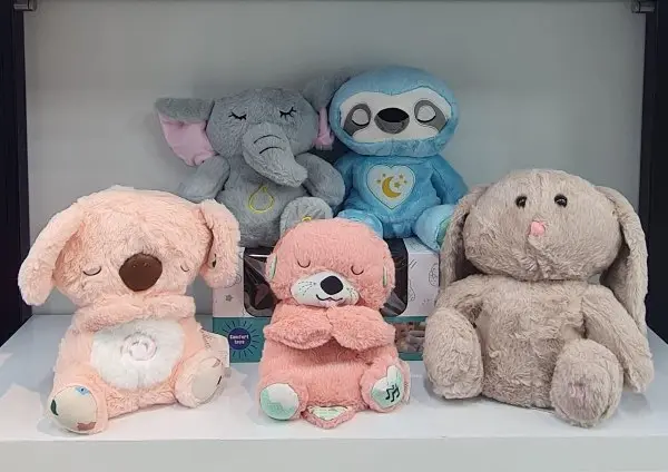 Cinco peluches con movimiento realista para dormir: un elefante gris, un perezoso azul, un koala rosado, una nutria rosada y un conejo beige en estante.