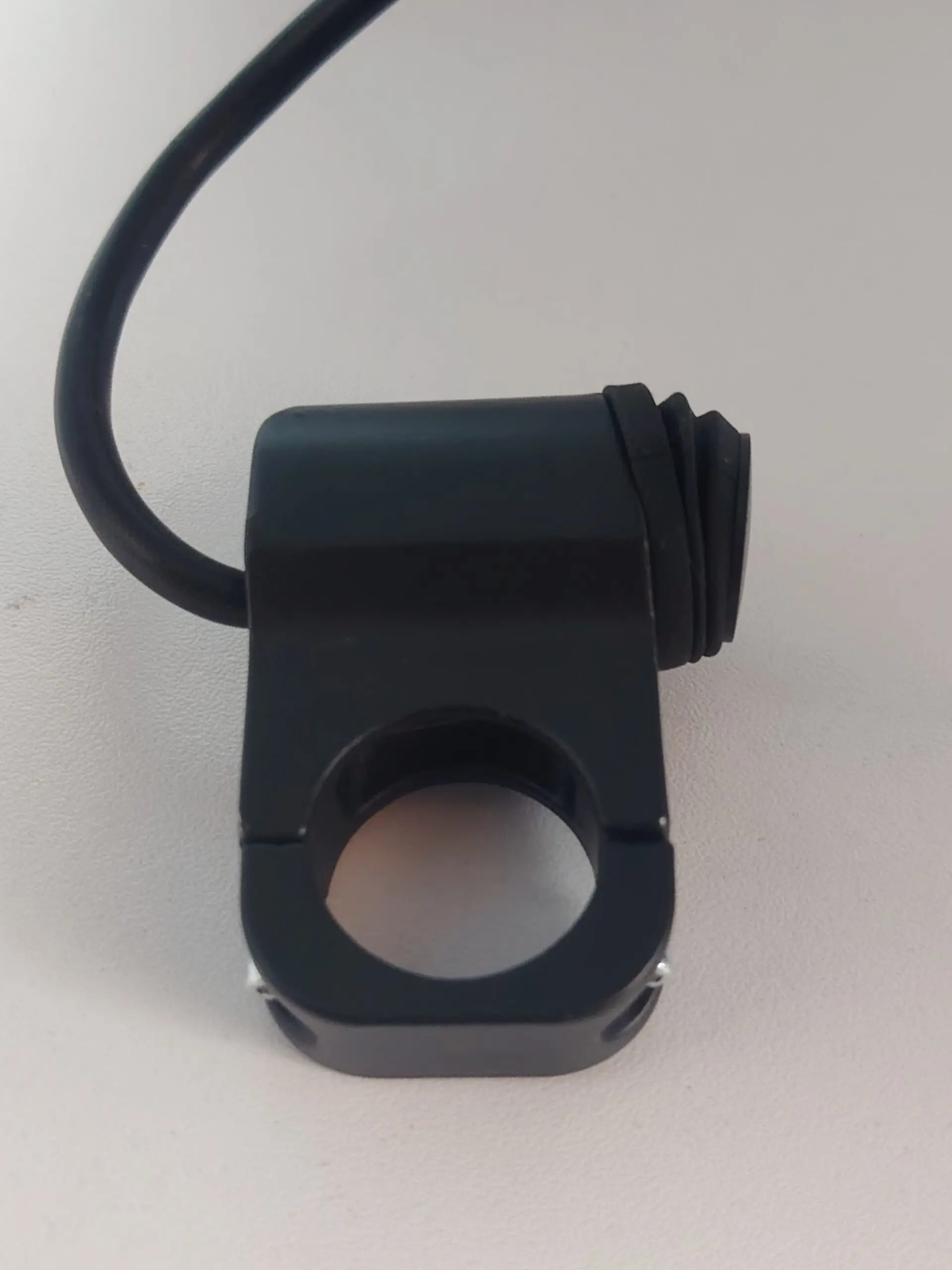 Interruptor de manillar negro con abrazadera circular ajustable, cable de conexión y botón de encendido con protector de goma.