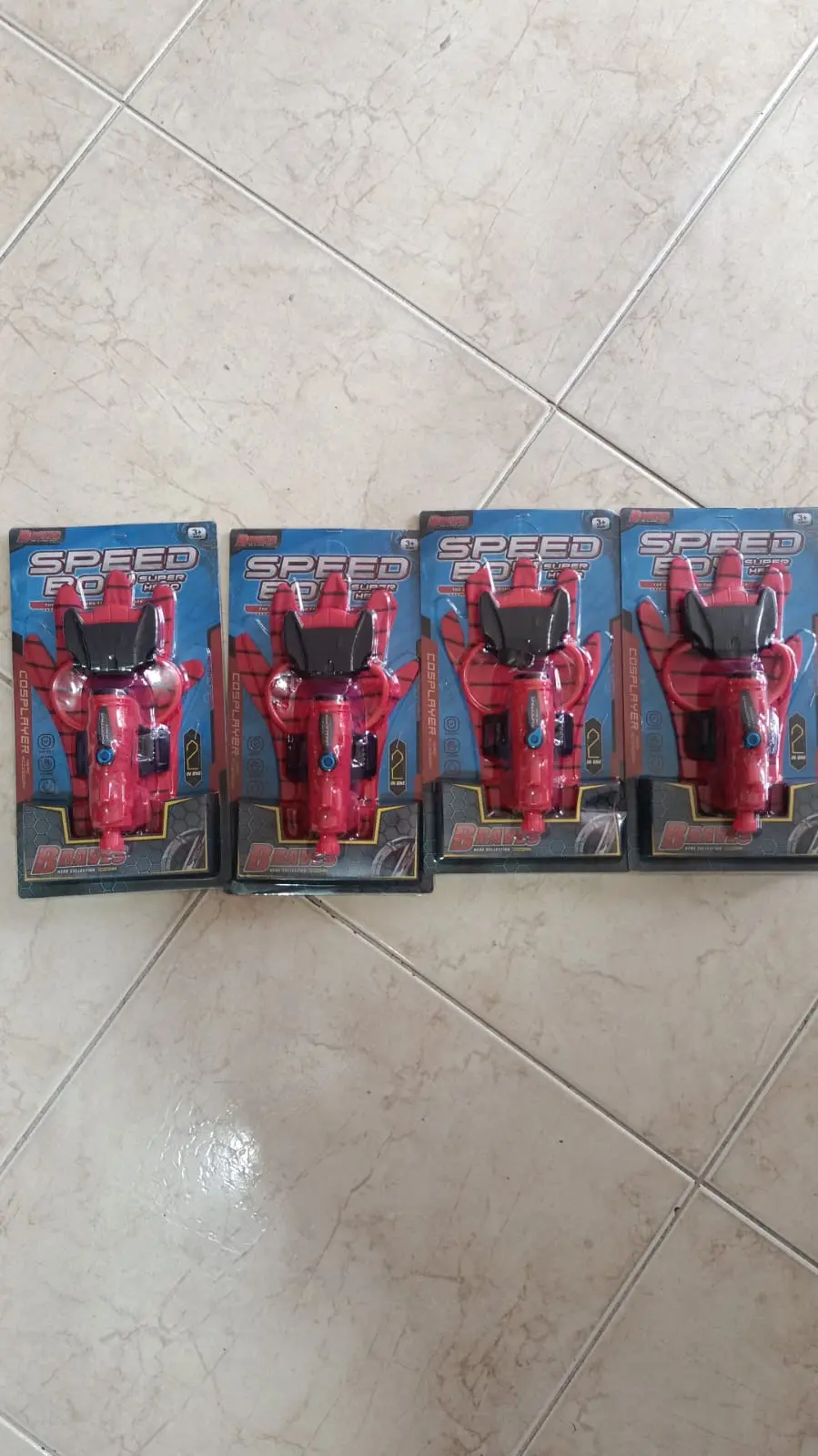 Cuatro guantes rojos lanzadores de agua para niños y cosplay de Spiderman en empaques originales sobre piso de cerámica.