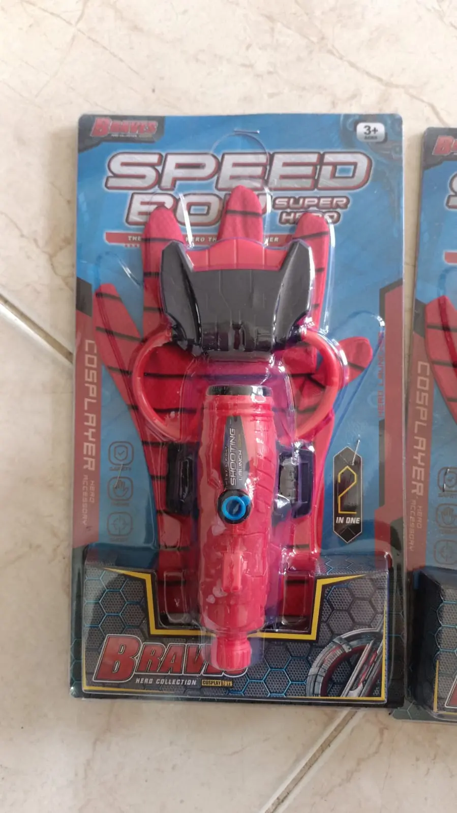 Guante de Spiderman rojo con telarañas negras y lanzador de agua con botón azul, en empaque de blíster para cosplay.