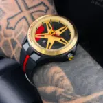 Reloj deportivo para hombre con correa de goma negra, caja dorada y esfera inspirada en rin de automóvil con detalles rojos.