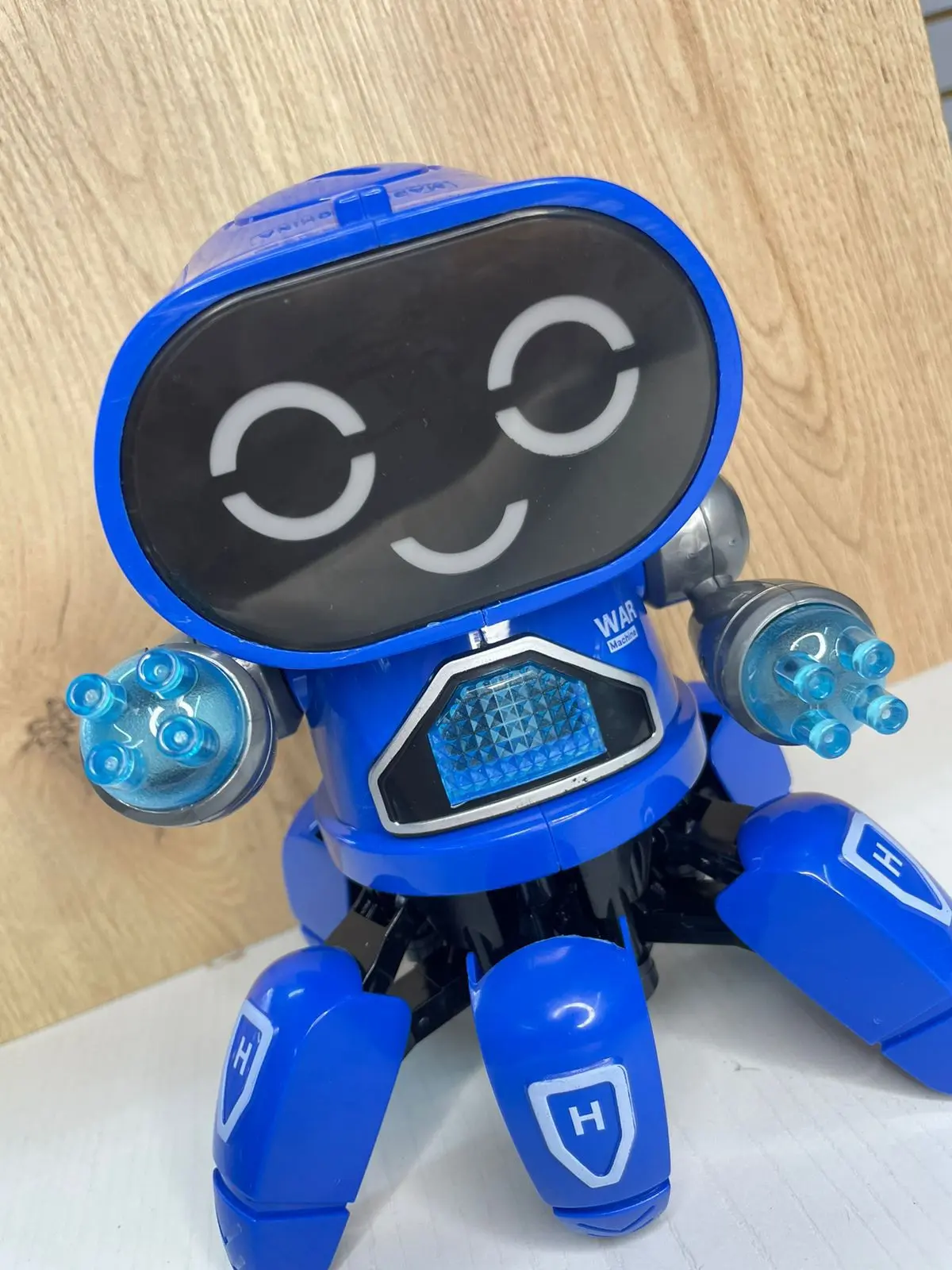 Robot juguete interactivo azul de seis patas con pantalla LED de ojos luminosos y manos translúcidas iluminadas.