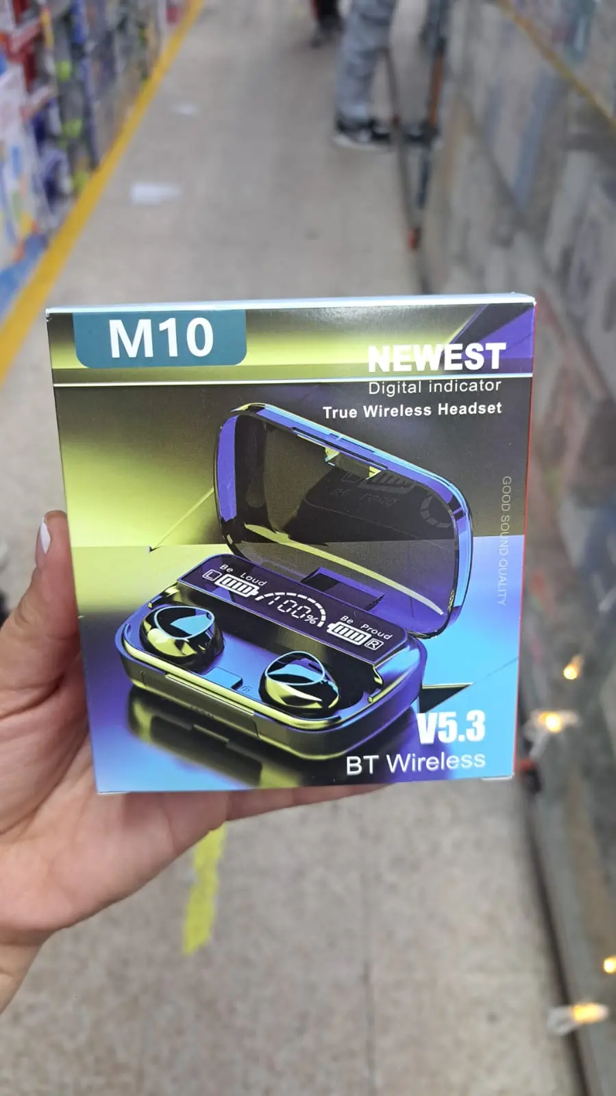 Caja de audífonos inalámbricos M10 V5.3 en mano, mostrando estuche azul con pantalla digital de batería y dos auriculares.