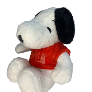 Peluche de Snoopy blanco con orejas negras y camiseta roja con la palabra Smiles, en posición sentada de perfil y textura suave.