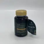 Frasco oscuro de Ashwagandha orgánica con tapa dorada y etiqueta colgante en forma de hoja con detalles botánicos sobre fondo neutro.