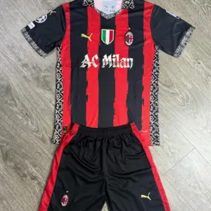 Conjunto de fútbol AC Milan negro y rojo con rayas verticales, cuello y detalles florales blancos, que incluye camiseta y pantaloneta doblados sobre superficie de madera.