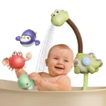 Bebé sonriente en tina jugando con ducha eléctrica verde de dinosaurio, incluye juguetes flotantes de cangrejo rojo, pingüino morado y ballena verde.