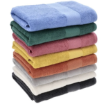 Pila de toallones de algodón premium en colores azul, verde, rosa, amarillo, naranja, gris, crema y negro, con textura suave de rizo.