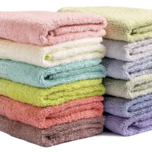 Dos pilas de toallones de algodón premium en tonos pastel y tierra, como rosa, verde, lila y coral, con textura suave y de alta absorción.