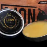 Set de dos latas de grasa nutritiva redondas con tapa plateada y contenido de cera amarilla clara para mantenimiento de cuero y botas sobre fondo de madera