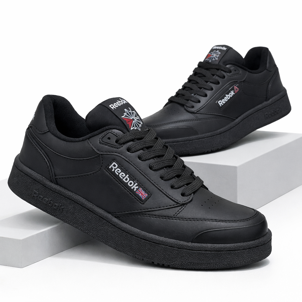 Zapatillas Reebok Club negras de corte bajo con textura de cuero sintético, cordones negros y logo blanco, sobre pedestales geométricos blancos.