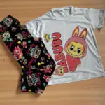 Pijama de dos piezas con camiseta blanca de manga corta con diseño de Labubu y leggings negros con estampado multicolor de personajes y estrellas.