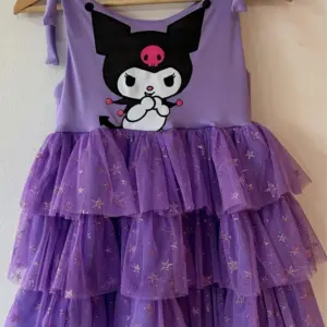 Vestido infantil lila con diseño de Kuromi, tirantes ajustables y falda escalonada de tul con brillo y estrellas doradas.