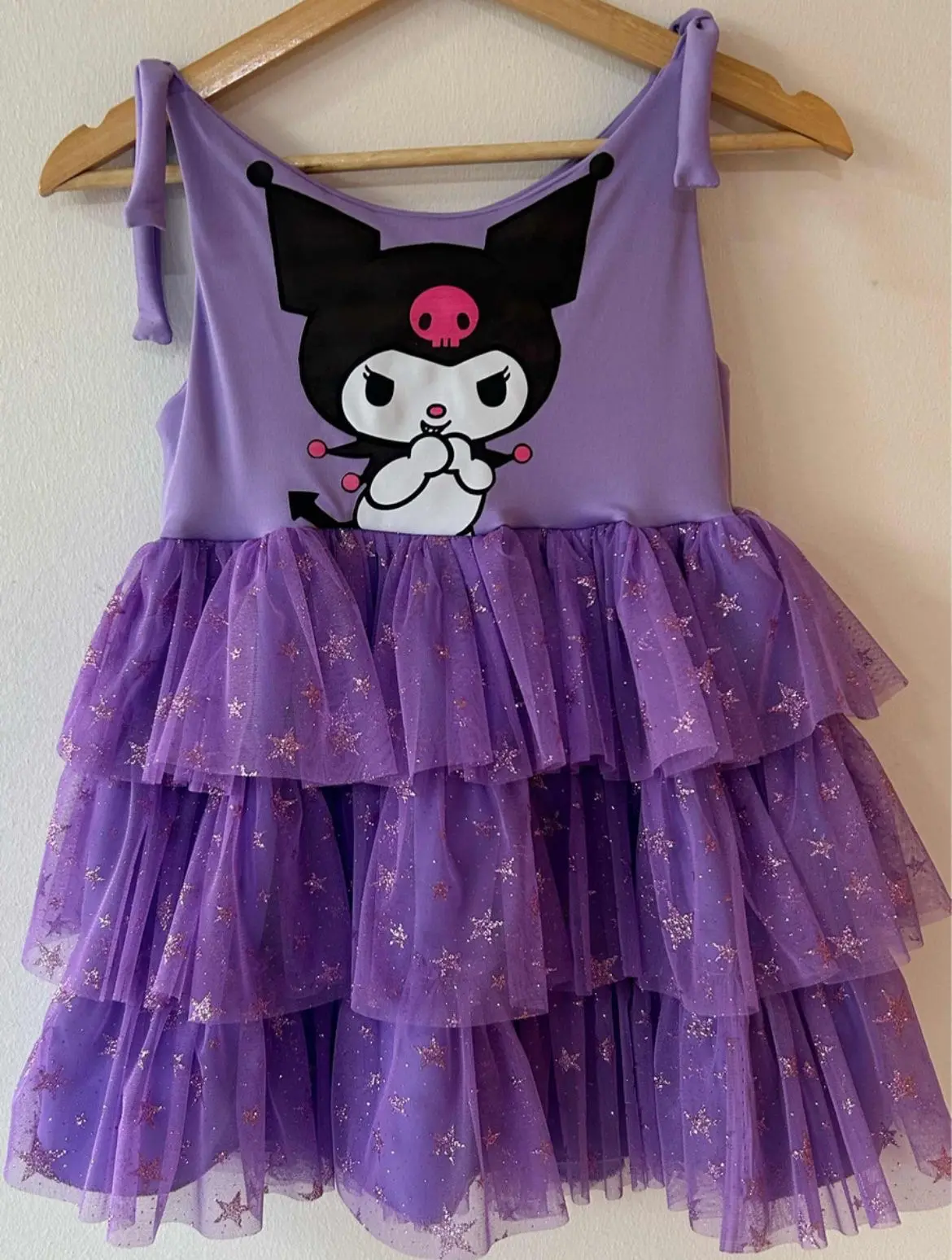 Vestido infantil lila con diseño de Kuromi, tirantes ajustables y falda escalonada de tul con brillo y estrellas doradas.