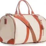Bolso de viaje beis con detalles en cuero caramelo, asas superiores, correa cruzada y cremalleras doradas.