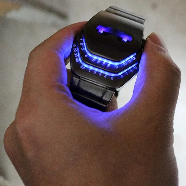 Reloj inteligente de metal oscuro con pantalla LED azul brillante y números digitales, sostenido por una mano para mostrar su diseño futurista.