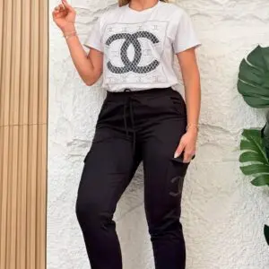Mujer de pie usando conjunto urbano de lycra negra con jogger cargo y blusón blanco con diseño frontal, zapatillas blancas y fondo texturizado.