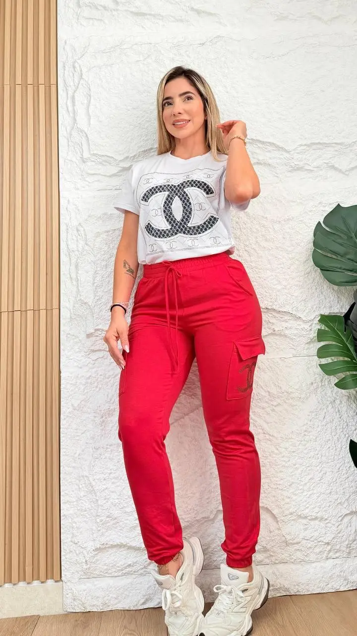 Mujer modelando conjunto jogger cargo rojo y blusón blanco con estampado y zapatillas blancas frente a pared texturizada.