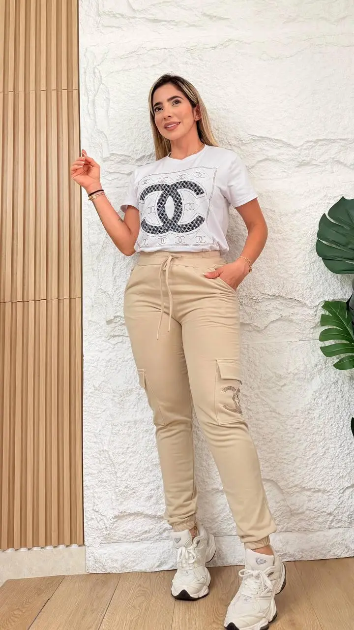 Mujer usando conjunto jogger cargo y blusón urbano en color beige y blanco, de lycra y burda gruesa con estampado, posando de pie en interior.