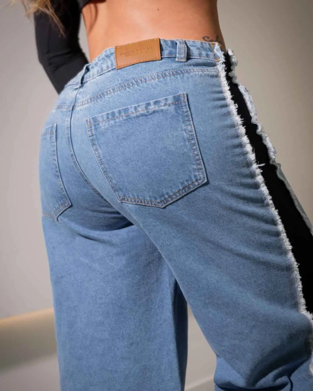 Pantalón jean azul de tiro alto, bota ancha, con bolsillos traseros y franja lateral negra con bordes deshilachados.