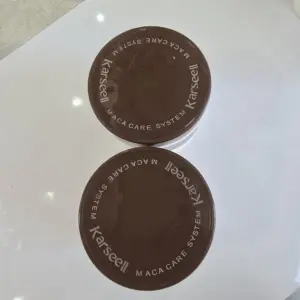 Dos envases circulares marrones de la mascarilla capilar Karseell Maca Care System con letras blancas sobre fondo blanco.