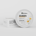 Crema aclarante de zonas oscuras de 85g en frasco circular blanco con tapa y caja de cartón, decorada con flores de manzanilla.