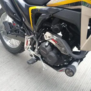Protector de mofle en acero inoxidable brillante instalado en el escape de una motocicleta, con diseño de ranuras para protección y estética.