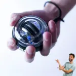 Mano sosteniendo ejercitador giroscópico transparente para muñeca con núcleo metálico y luz azul interior para fortalecer antebrazos.