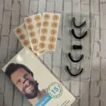 Kit de inicio para ronquidos sobre fondo de ladrillo, incluye caja con modelo, láminas de cintas adhesivas circulares y estuche con cinco dilatadores nasales de silicona negra en diferentes tamaños.