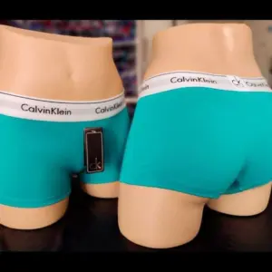Cacheteros turquesa Calvin Klein para dama, mostrados en maniquíes de torso en vista frontal y posterior con banda elástica blanca con logo.
