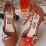 Zapatos cerrados de tacón bajo color canela con textura de gamuza, estampado floral rojo en la punta y correa con hebilla dorada.