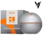 Perfume masculino Hugo Boss In Motion Original en frasco esférico plateado con detalles naranjas, junto a su caja gris de 90 ml.