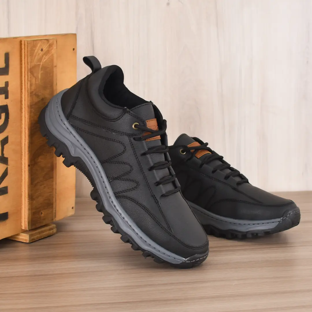 Tenis híbridos negros Urbots Ride de cuero texturizado con suela gruesa gris de alta tracción, exhibidos sobre superficie de madera.