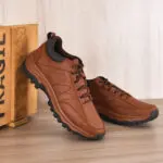 Tenis híbridos marrones de cuero sintético con suela dentada negra, inclinados junto a una caja de madera sobre superficie de madera.