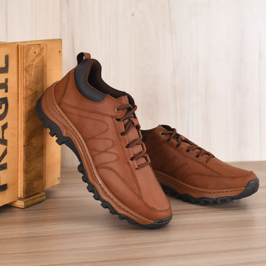 Tenis híbridos marrones de cuero sintético con suela dentada negra, inclinados junto a una caja de madera sobre superficie de madera.