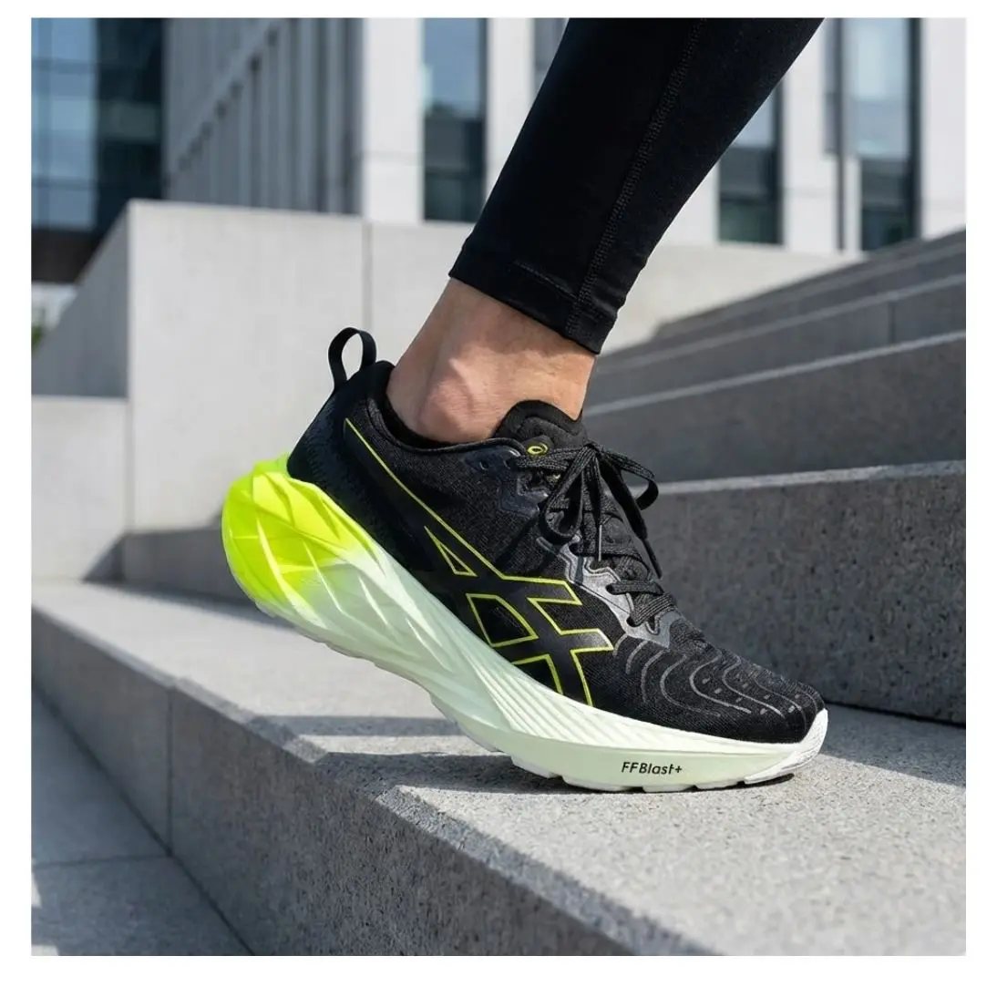 Zapatilla Asics Novablast negra con suela alta verde neón para running y uso urbano, sobre escalones de concreto.