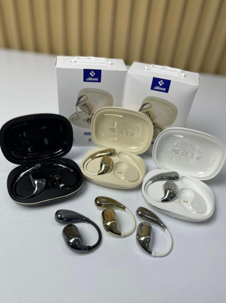 Audífonos inalámbricos ergonómicos en negro, dorado y blanco, con estuches de carga abiertos y cajas de empaque al fondo.