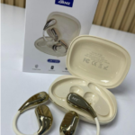Audífonos inalámbricos ergonómicos con acabado dorado metálico, ganchos color crema, estuche de carga abierto y caja del producto.