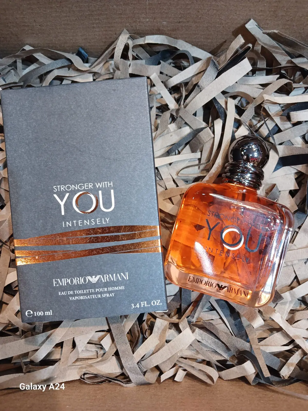 Perfume Emporio Armani Stronger With You Intensely 100 ml y su caja gris con detalles cobrizos sobre papel triturado.
