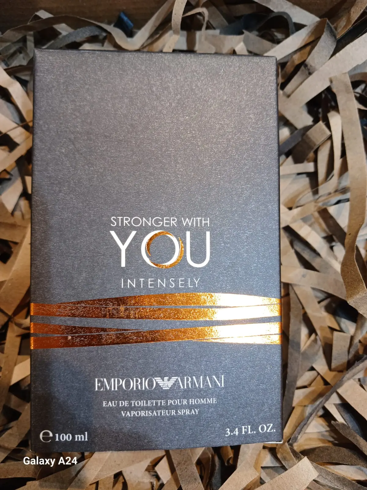 Caja gris oscuro con textura de Emporio Armani Stronger With You Intensely, acentos dorados y 100 ml sobre papel picado.