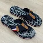 Par de sandalias thong para mujer con estampado geométrico en blanco y negro, tiras de tela azul oscuro con detalles en marrón y franja tricolor, sobre superficie de madera.