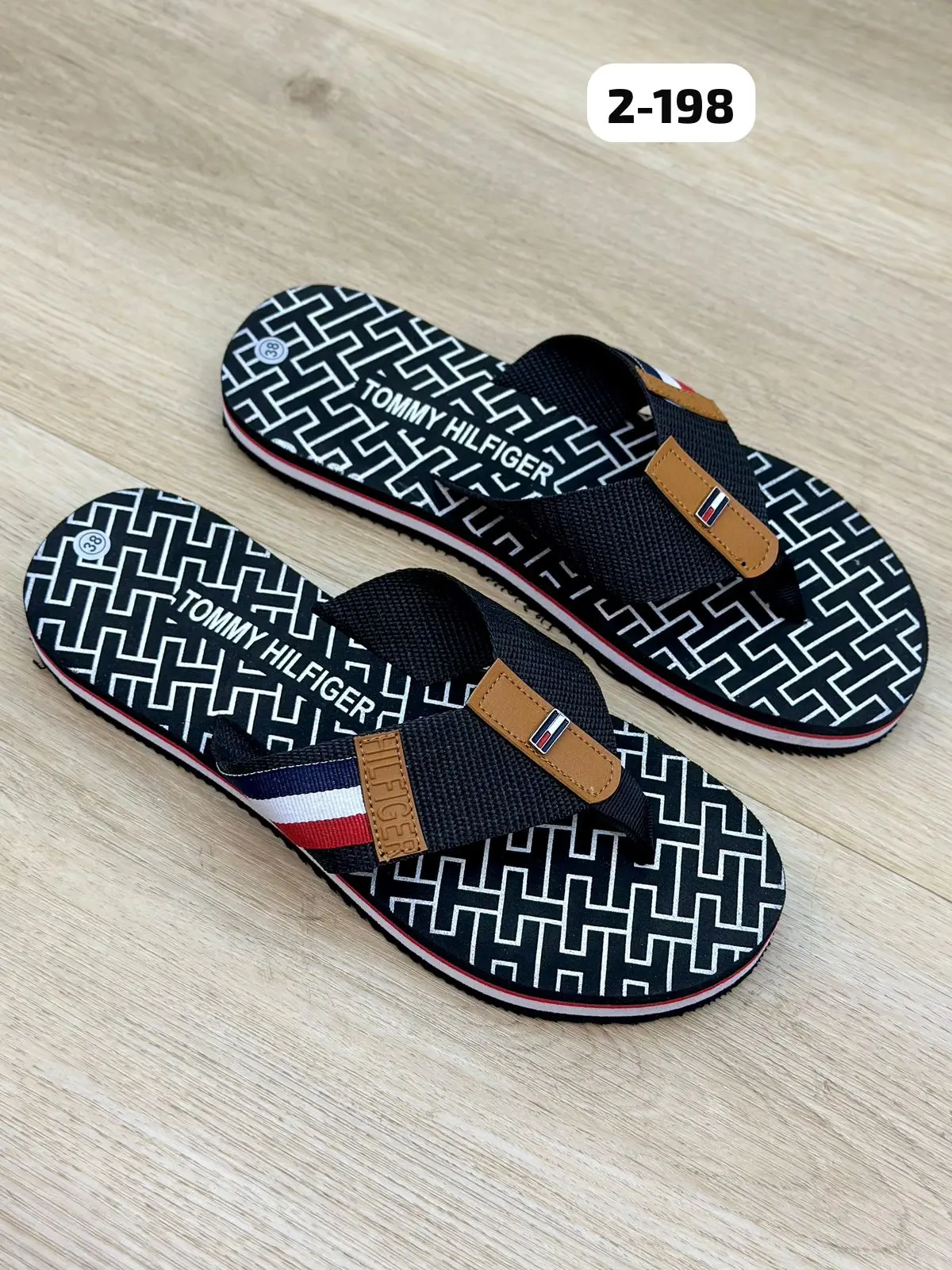 Par de sandalias thong para mujer con estampado geométrico en blanco y negro, tiras de tela azul oscuro con detalles en marrón y franja tricolor, sobre superficie de madera.