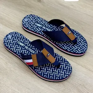 Sandalias Tommy Hilfiger para dama, diseño thong en azul marino con monograma blanco, correa de tela azul, detalle marrón y suela tricolor.