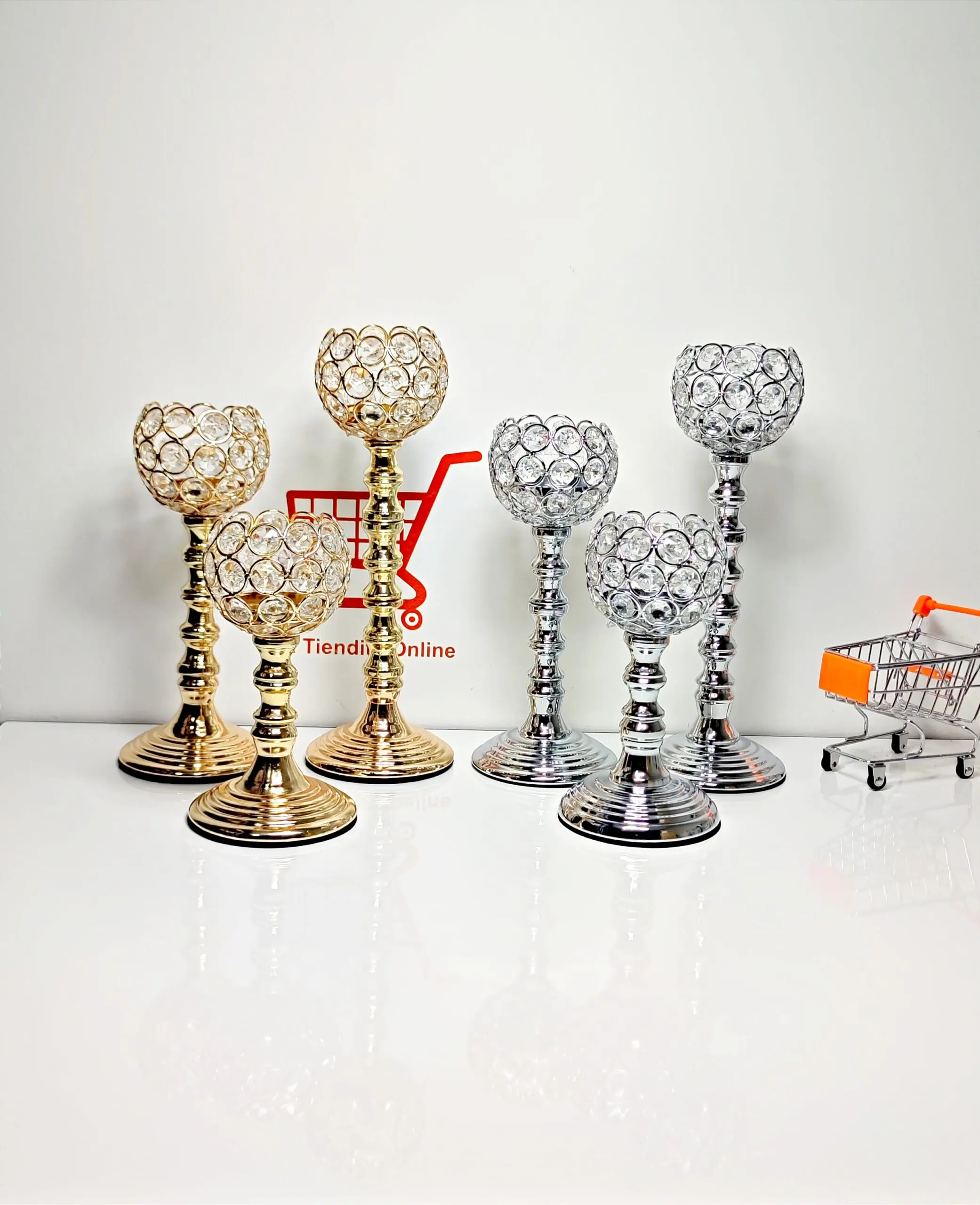 Set de tres candelabros de cristal y metal con acabado brillante, dos en tonos dorados y tres plateados, dispuestos sobre una superficie blanca.