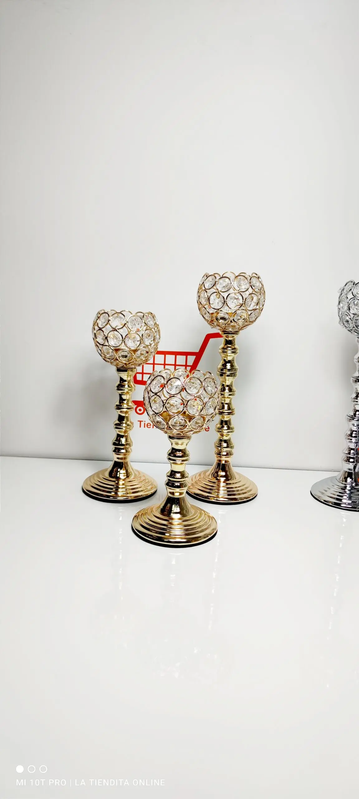 Set de tres candelabros dorados de metal y cristal con copas decorativas de cuentas brillantes, dispuestos en diferentes alturas sobre una superficie blanca.