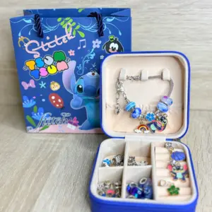Set de manilla plateada con dijes coloridos en estuche rígido azul abierto, compartimentos con accesorios y bolsa de regalo temática de Stitch.