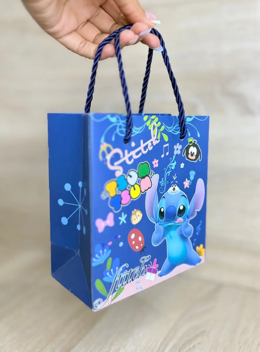 Estuche azul con diseño de Stitch y motivos coloridos, con asas de cuerda, sostenido por una mano sobre superficie de madera.