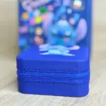 Estuche rígido azul cuadrado con de Stitch sobre superficie de madera y bolsa de regalo temática al fondo