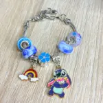 Manilla de cadena plateada con cuentas azules y blancas, dijes de flor azul, arcoíris y Stitch, sobre fondo de madera clara.